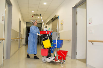 Full length of female cleaner working at corridor in hospital