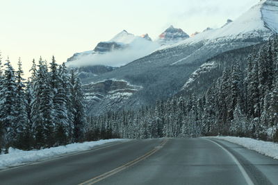 Road by snowcapped mountains against sky during winter