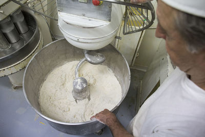 Baker observing the bread dough being kneaded in an industrial mixer