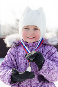 Portrait of cute girl holding medal while standing outdoors during winter