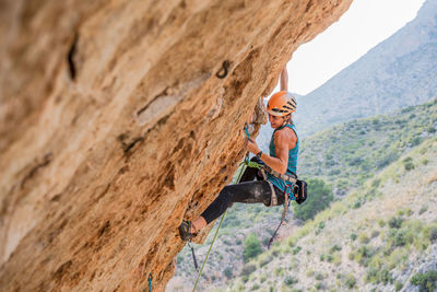 From below side view of active focused youthful female alpinist climbing on cliff in summer day