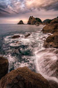 Scenic view of rocks beach against cloudy sky during sunset