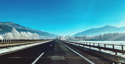 Road leading towards mountains against blue sky