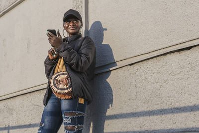 Woman stands outside against a wall during the sunset and waits with a mobile phone in her hand