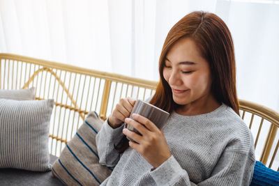 Young woman using mobile phone while sitting on sofa at home