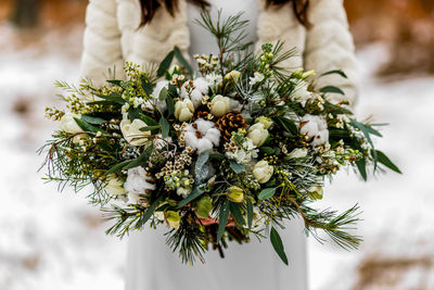 Bride holding a white wedding bouquet during a wedding ceremony in winter on snow in the middle of a forest covered with fresh snow