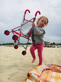 Full length of girl holding stroller while walking at beach against sky