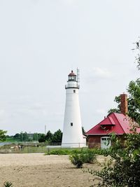 Lighthouse amidst trees and buildings against sky