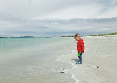 Boy standing on beach against sky