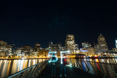 Women making light painting while standing on footbridge at night