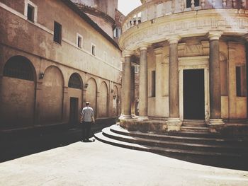 Rear view of man walking on street amidst building in city