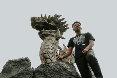 Low angle view of smiling young man on rock against clear sky