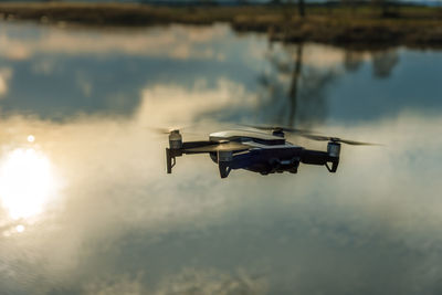 Small modern drone hovering taking picture of sunset.