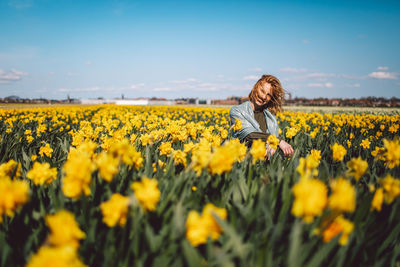 Scenic view of girl sitting on a narcissus field against sky