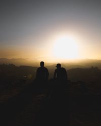 Silhouette men sitting against sky during sunset