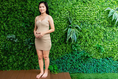 Portrait of pregnant young woman standing against plants