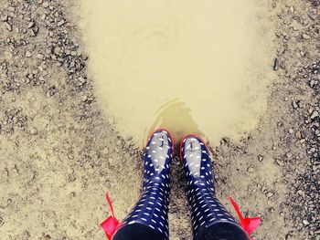 Low section of woman wearing rubber boots by puddle