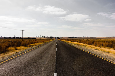 Empty road amidst field against sky