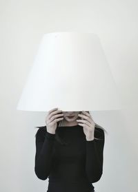Woman wearing lamp shade while standing against white background