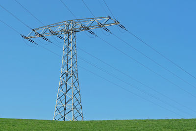 Low angle view of electricity pylon on field against clear sky