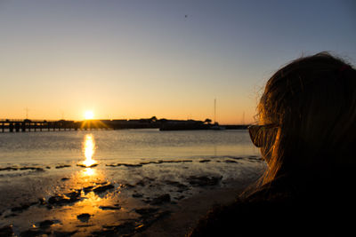 Rear view of woman at beach against sky during sunset