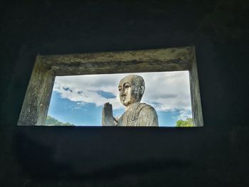 Low angle view of sculpture against sky seen through window