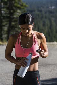 Tired athlete holding water bottle while standing on footpath