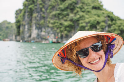 Smiling woman wearing hat and sunglasses by sea