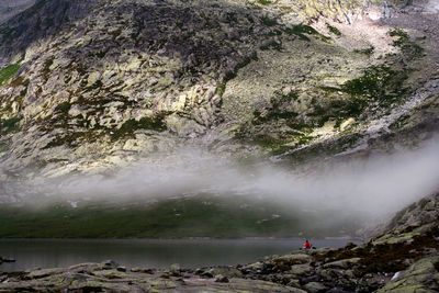 Rear view of woman standing on rock by waterfall