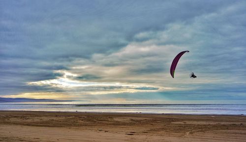 Parachute flying over sea against cloudy sky