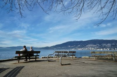 Men sitting on seat at shore against sky