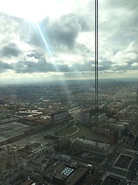 Aerial view of cityscape against cloudy sky on sunny day