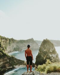 Rear view of shirtless man looking at mountains against clear sky