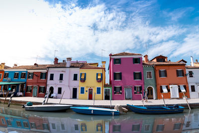 Boats moored in canal by buildings against sky