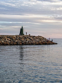 Lighthouse by sea against sky during sunset