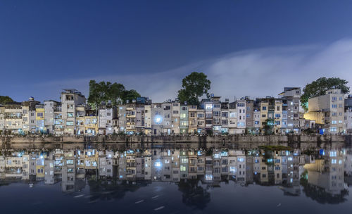 Buildings by lake against sky in city at night