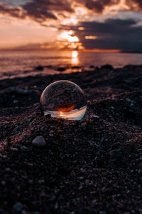 Close-up of crystal ball at beach against sky during sunset