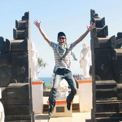 Full length portrait of happy man with arms raised against sky