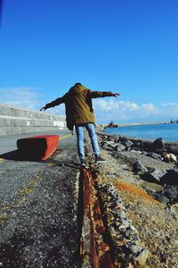 Rear view of man standing by sea against blue sky