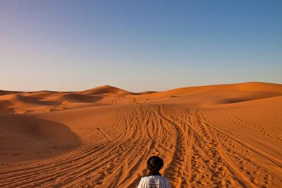 Rear view of man in desert against clear sky