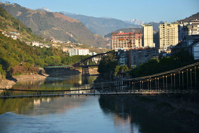 Bridge over river by buildings in city against sky