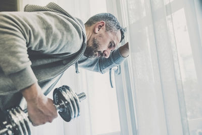 Sporty man working out and trains at home. fit boy doing exercises for biceps in the living room. 