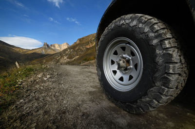 Close-up a large off-road all-terrain car wheel stands on a rough road in the mountains