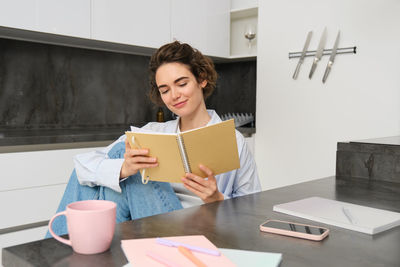 Portrait of young woman using digital tablet while sitting on table