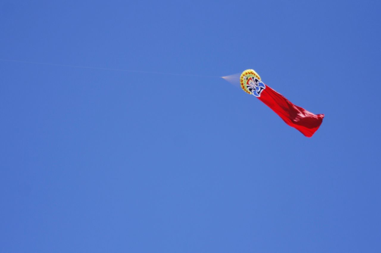 clear sky, copy space, blue, low angle view, red, flag, patriotism, national flag, mid-air, identity, day, wind, no people, outdoors, freedom, flying, sunlight, adventure, parachute, american flag