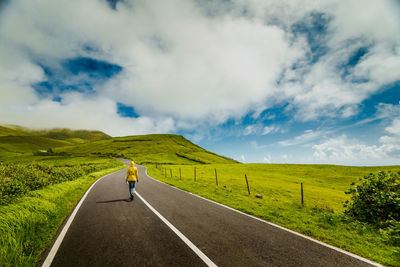 Rear view of woman walking on mountain road against cloudy sky