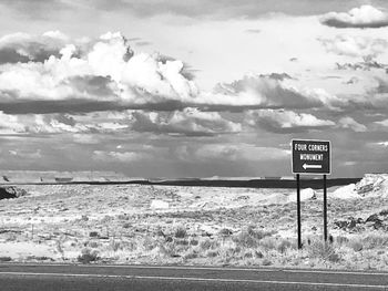 Road sign by sea against sky