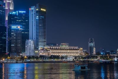 Illuminated buildings by river against sky at night