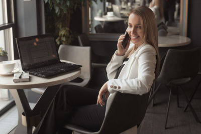 Smiling businesswoman talking on phone while sitting at cafe