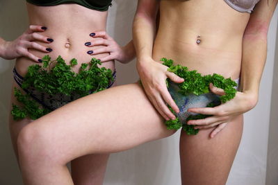 Midsection of female friends with cilantro in panty standing against wall